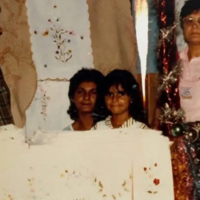 Duas meninas sorriem atrás de toalhas bordadas com flores, numa foto antiga de cores desbotadas.